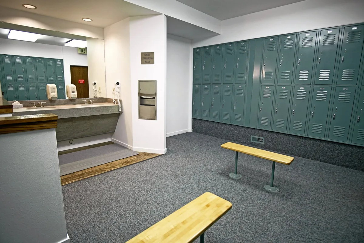A practical locker and vanity area with benches, designed for changing clothes and organizing personal items in a tidy, shared environment. The neutral tones and ample storage evoke a sense of orderliness and cleanliness.