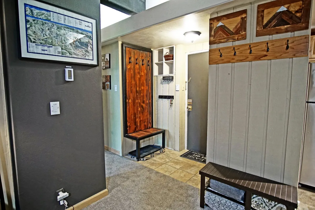 This image captures a cozy entryway with a wooden bench, coat hooks, decorative wall art, and the entry door. The space is designed for greeting guests, hanging coats, and storing shoes, offering a sense of warmth and practicality right as you enter the home.
