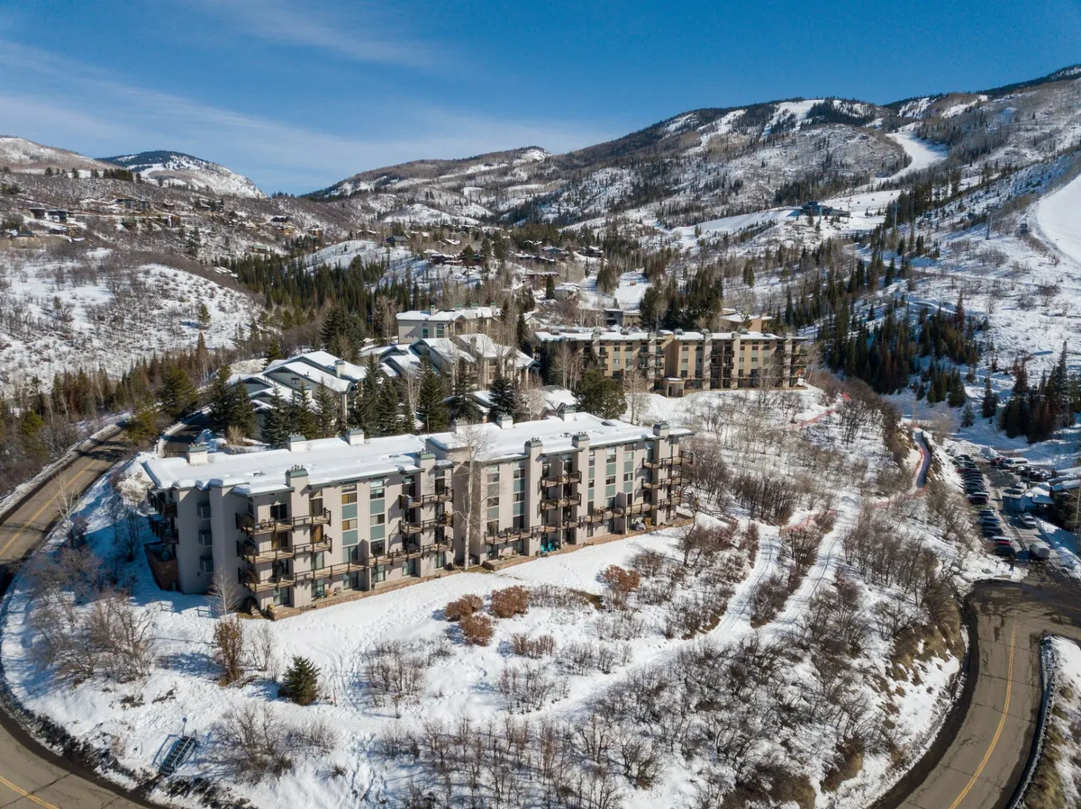 A striking exterior view of the property with modern architectural lines, set against snow-covered mountains and a winding road. The winter landscape highlights access to outdoor recreation and the natural beauty surrounding the resort.