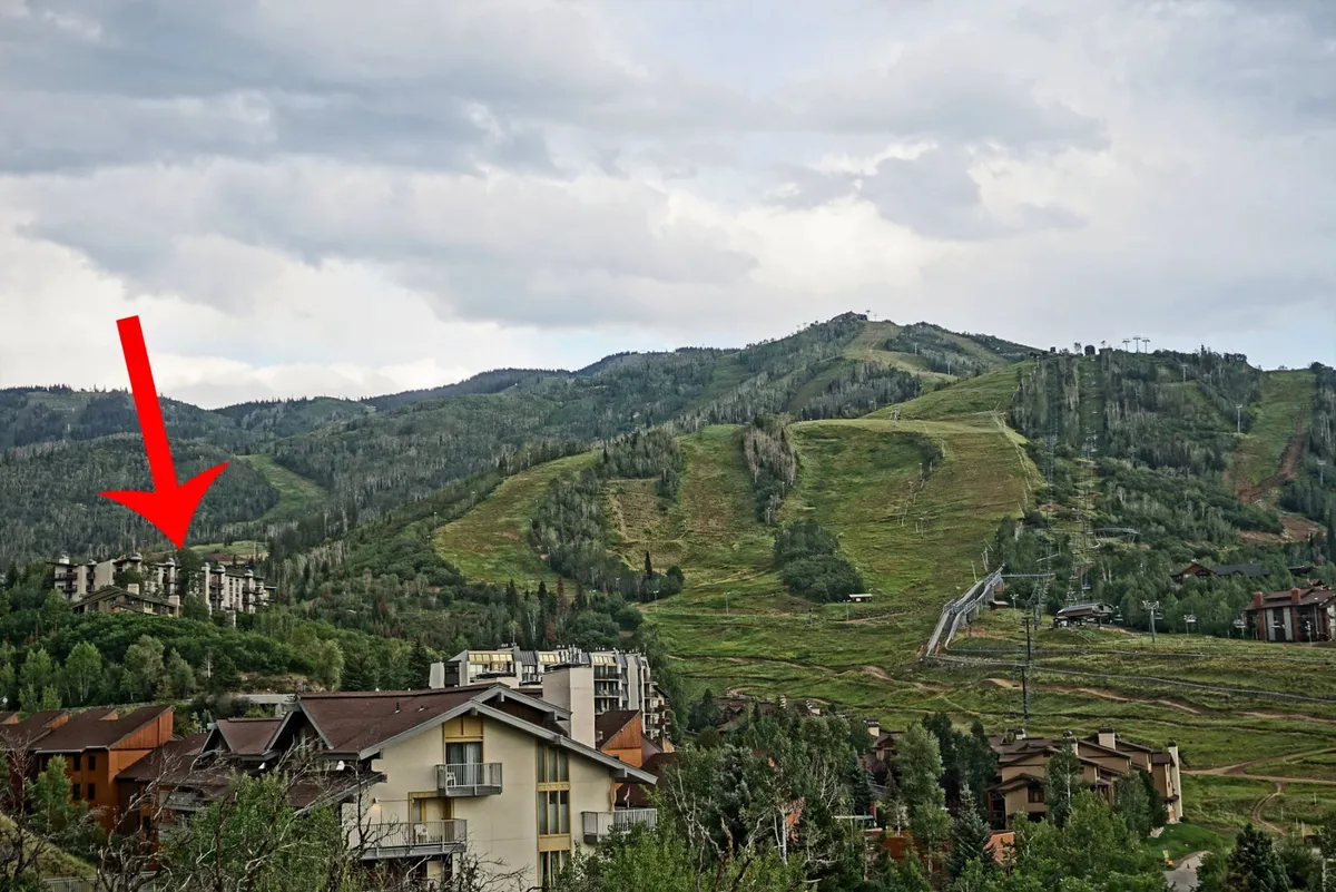 The image captures a serene exterior view of the condo complex nestled among lush forested areas, with majestic mountain ranges rising in the background. The tranquil setting hints at easy access to hiking and skiing, with the natural beauty of Steamboat Springs visible throughout. The residential buildings blend harmoniously with the landscape, suggesting a peaceful retreat after an adventurous day outdoors.