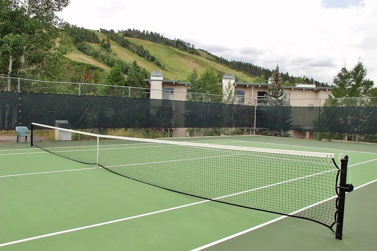 This exterior shot shows a well-maintained tennis court framed by lush green trees and hills in the background. The net and court surface evoke energy and recreation, while the natural surroundings connect guests to the outdoors.